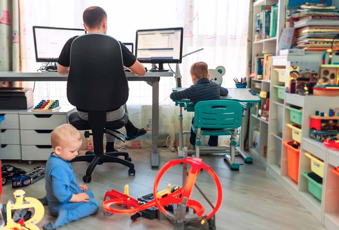 Hombre sentado en escritorio de su casa con sus hijos jugando al lado